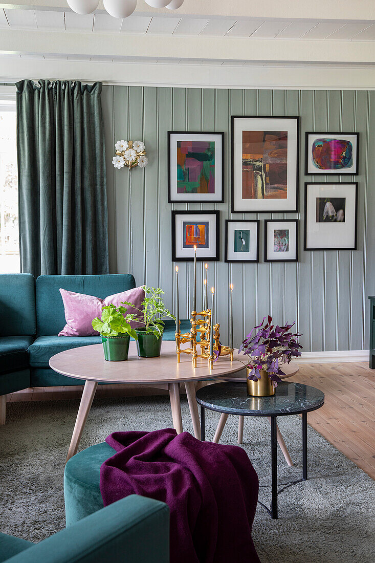 Living room with green velvet sofa, pastel-coloured wooden table and picture wall in shades of green and purple