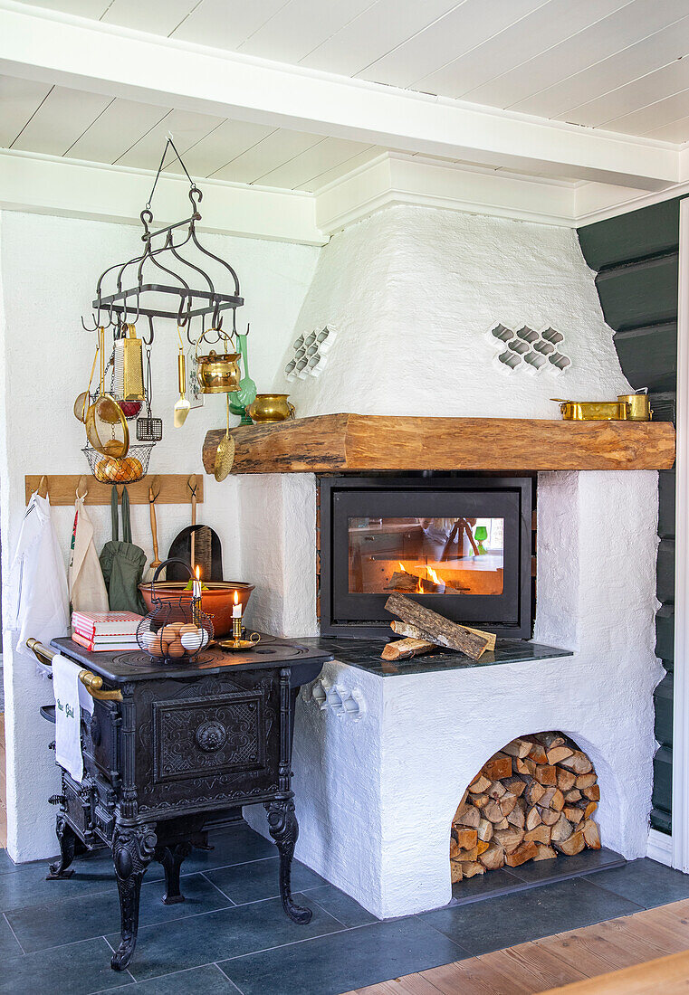 Cosy corner with wood-burning stove, kitchen utensils and firewood in country-style kitchen