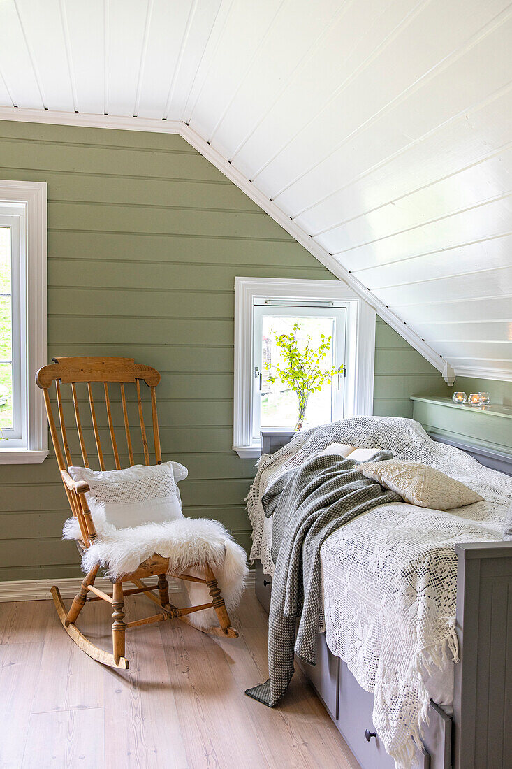 Bedroom under the roof with wooden rocking chair and bed