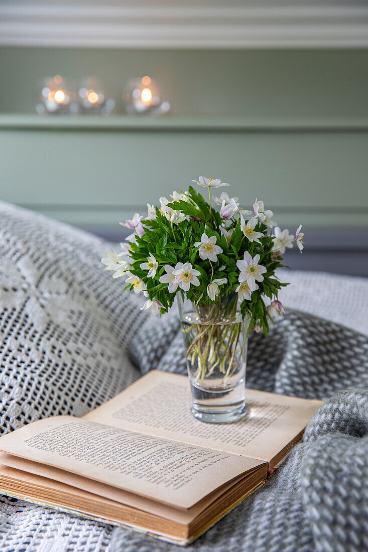 Vase mit Frühlingsblumenstrauß steht auf geöffnetem Buch im Schlafzimmer