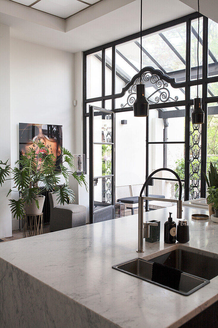 Light-colored kitchen with marble worktop and large windows made of a glass and steel construction