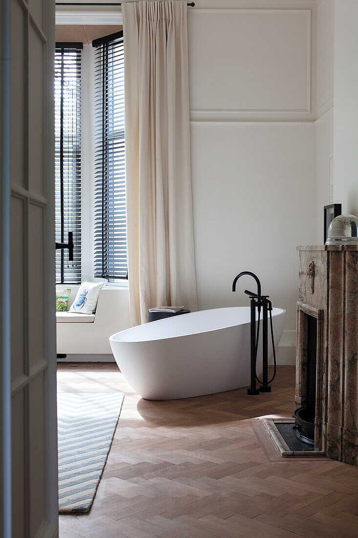 Freistehende Badewanne vor Erkerfenster mit Holzjalousien im eleganten Badezimmer