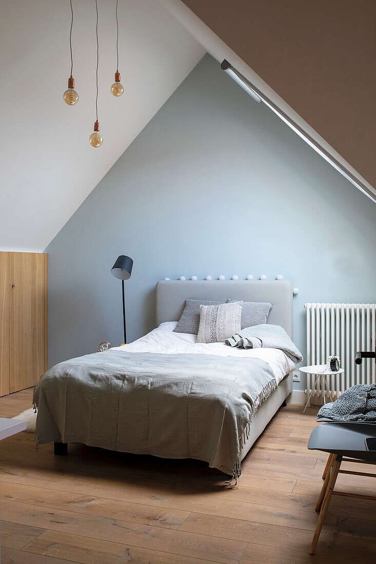 Attic bedroom with wooden floor and grey upholstered bed