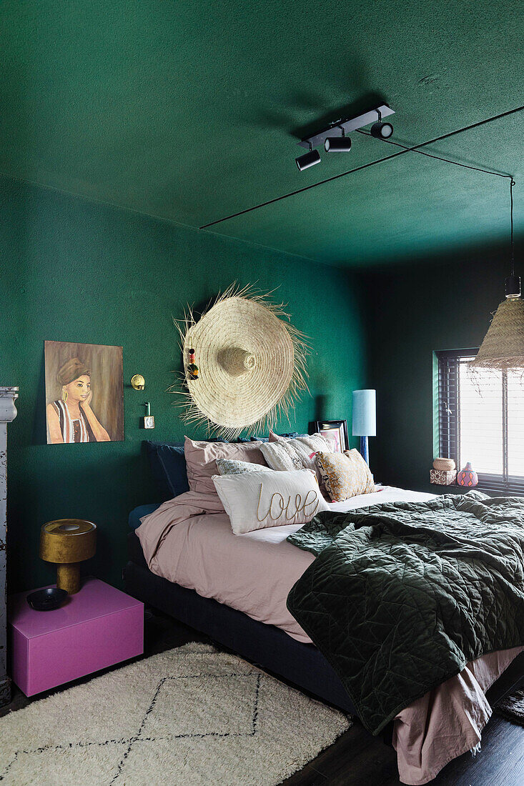 Bedroom with walls and ceiling in green, straw hat decor and pink bedside table