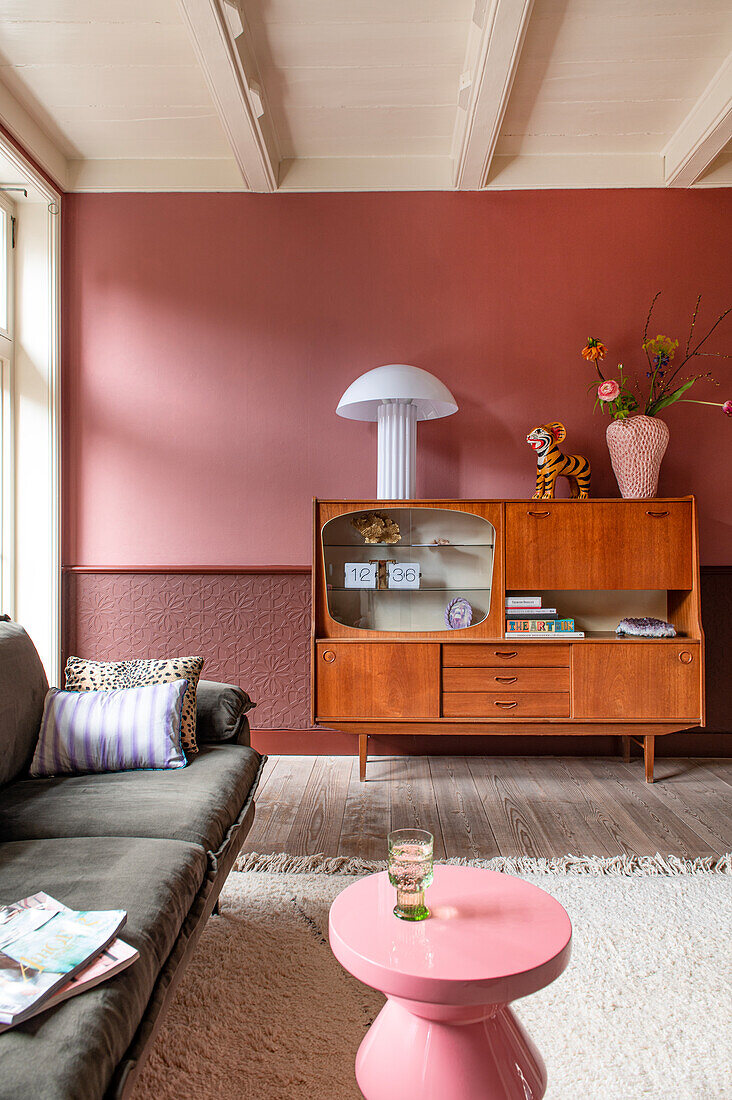 Wohnzimmer mit Vintage-Holzschrank, rosafarbener Akzentwand und Beistelltisch in Rosa