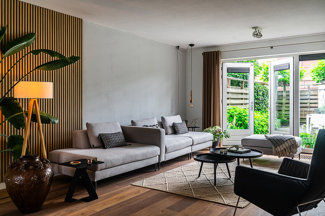 Wohnzimmer mit grauen Sofas, Akzentwand aus Holz und Blick in den Garten