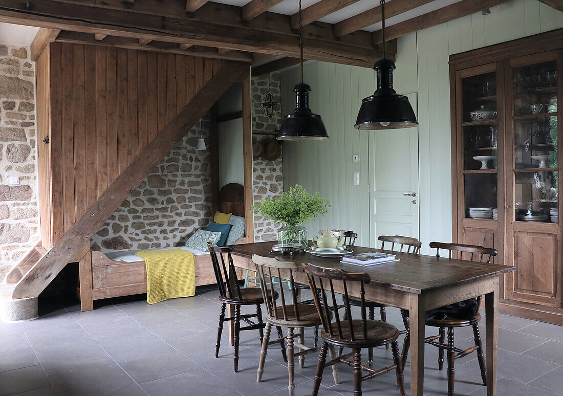 Dining area with wooden table and rustic country-style chairs, sleeping alcove under wooden staircase