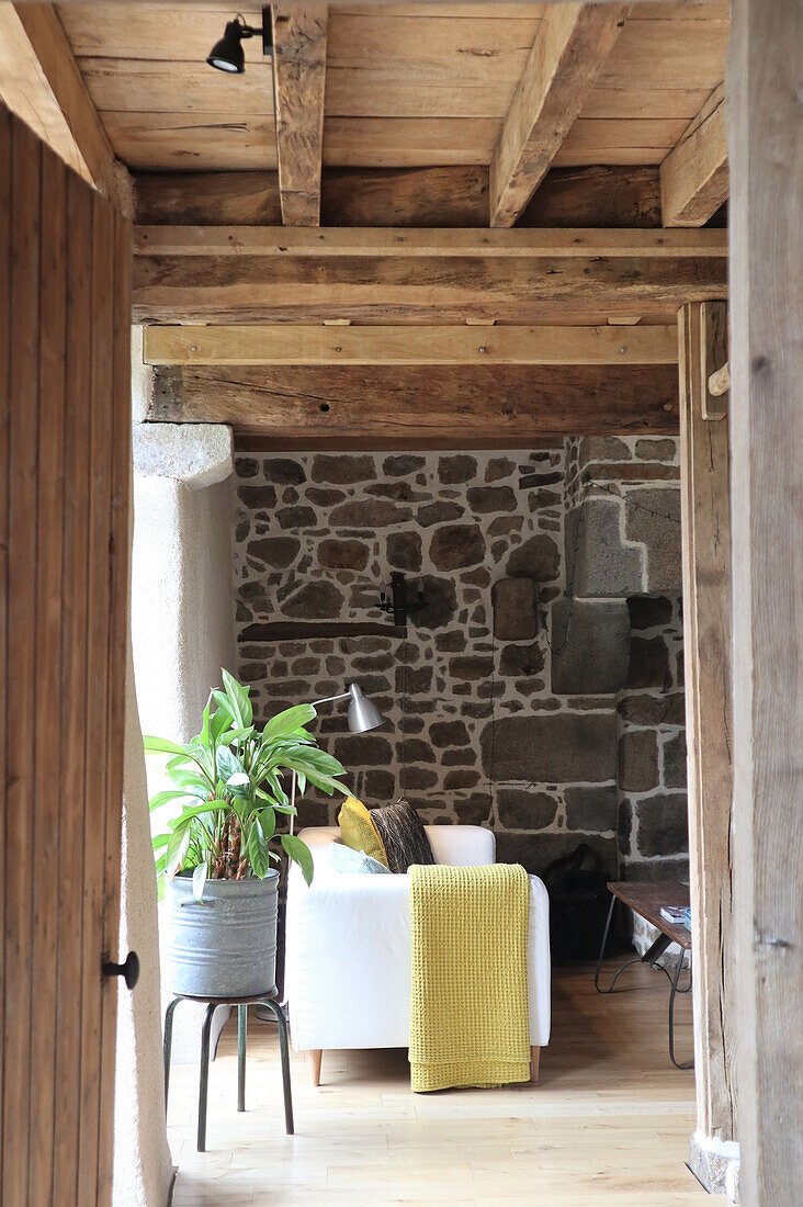 View of living room with couch, natural stone wall and wooden beamed ceiling