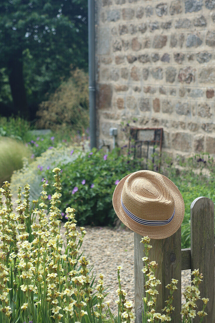 Straw hat on garden fence, blooming summer flowers