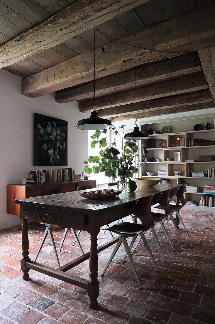 Rustic dining room with wooden table, modern chairs, wooden beamed ceiling and brick floor