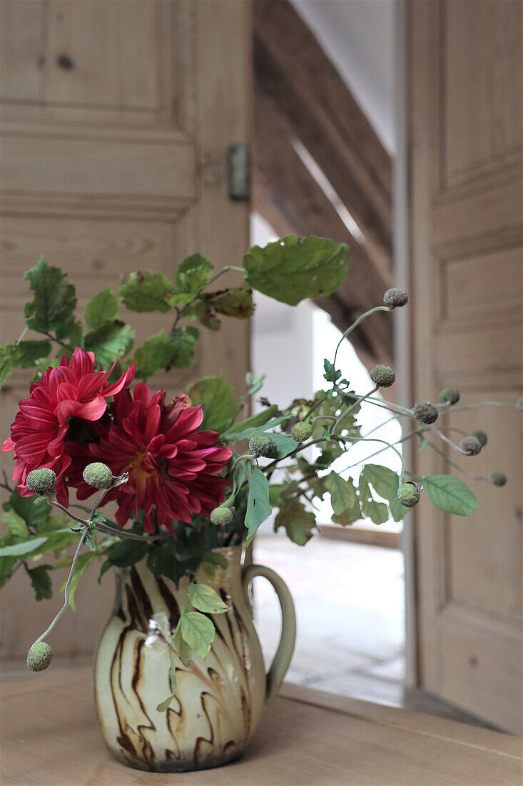 Strauß mit roten Dahlien (Dahlia) in Keramikkrug vor Holztür