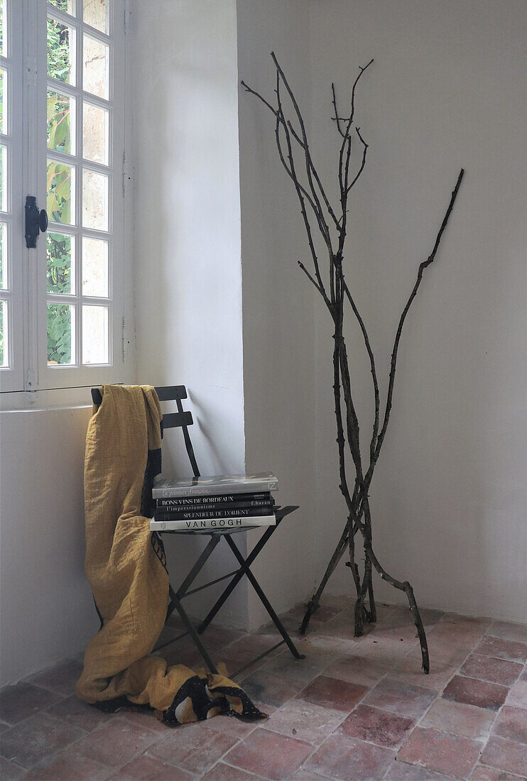 Minimalist decorated corner with branches, chair, stack of books and yellow cloth