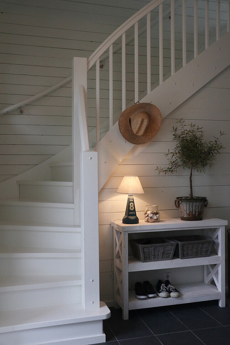 Wooden staircase painted white, straw hat, sideboard with decoration and shoes