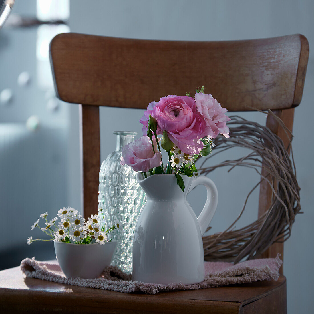 Vase with pink ranunculus and camomile flowers on a wooden chair