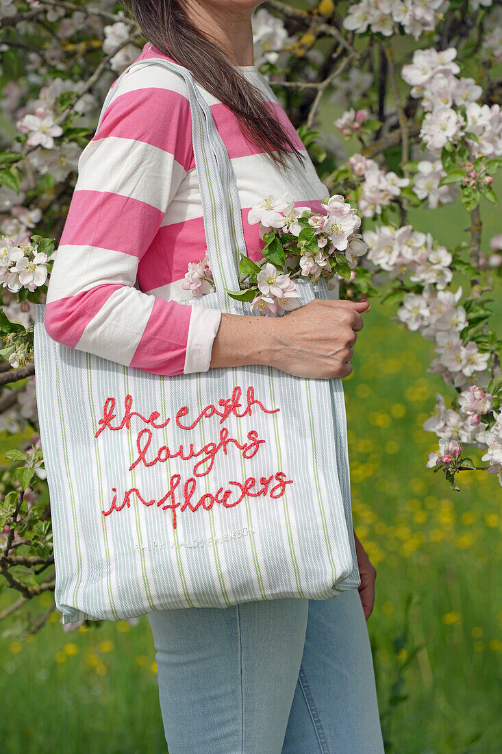 Woman with embroidered bag in front of blossoming apple tree