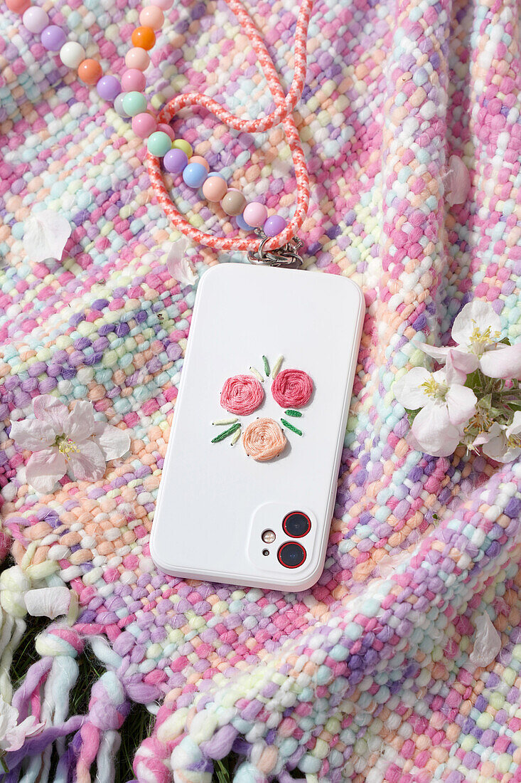 Mobile phone case with floral embroidery on pastel-coloured blanket