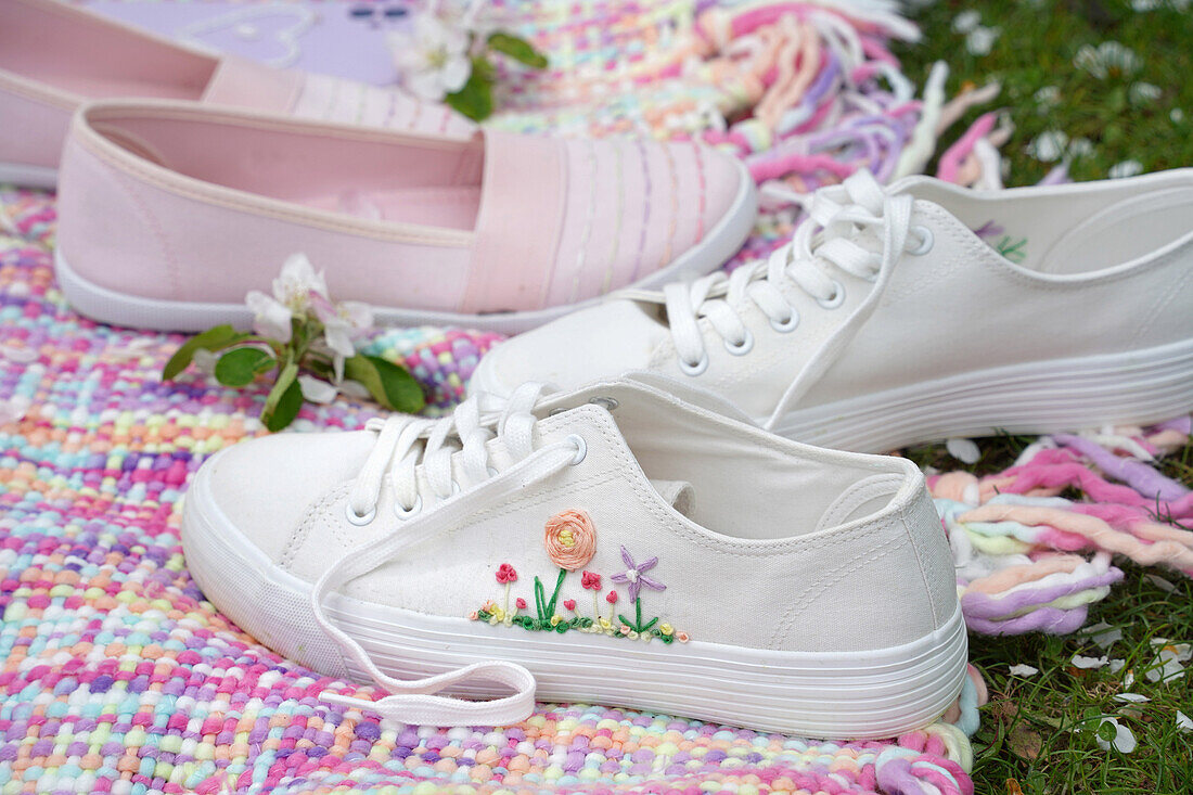 White trainers with floral embroidery and embroidered slippers on a colourful blanket in the garden