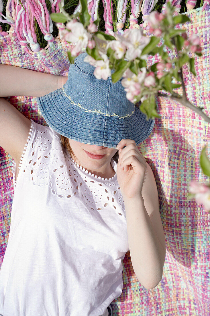 Woman in denim hat lying on colourful picnic blanket under blossoming apple tree