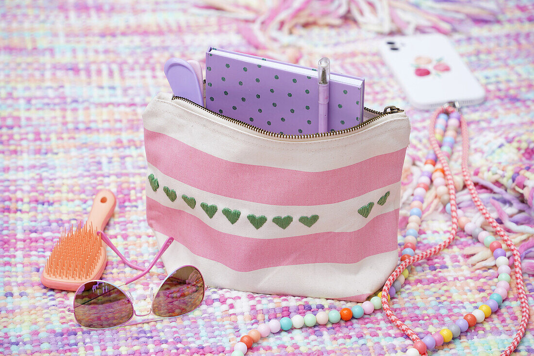 Cosmetic bag with stripes and hearts, notebook, sunglasses and brush on colourful blanket