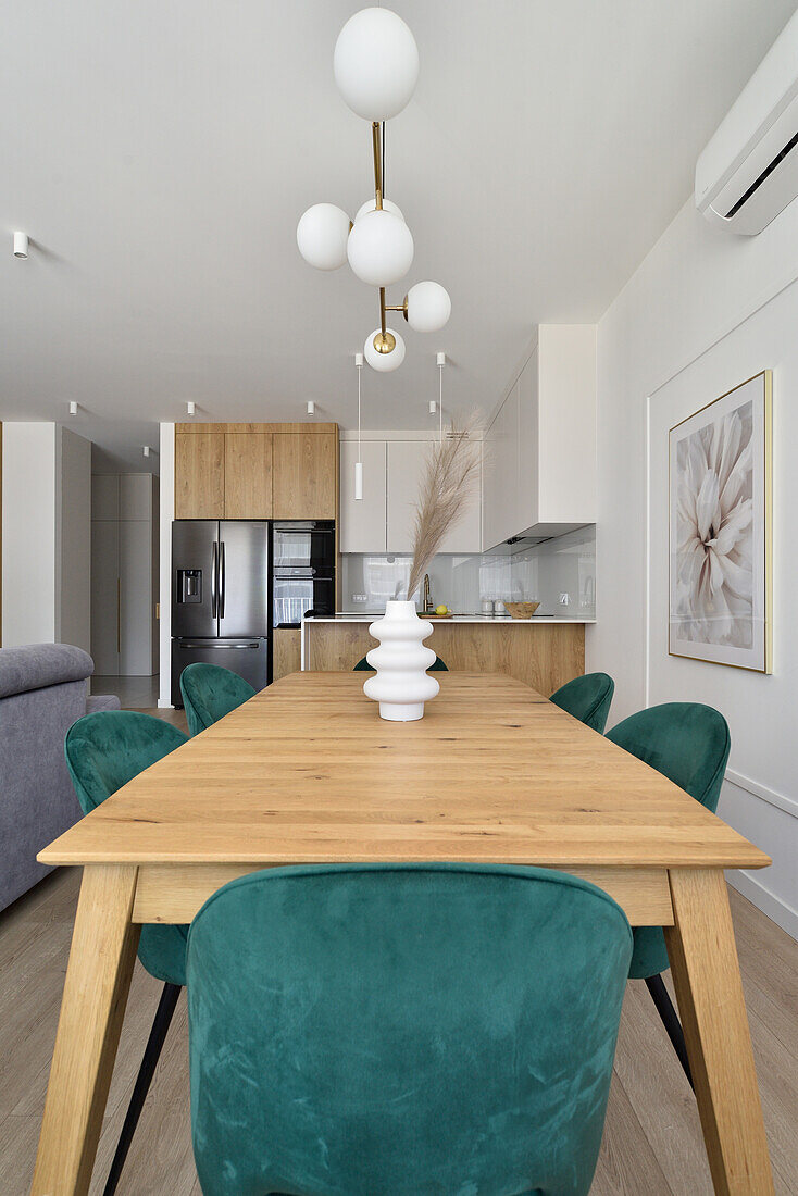 Wooden table with green velvet chairs in modern kitchen with wooden cupboards