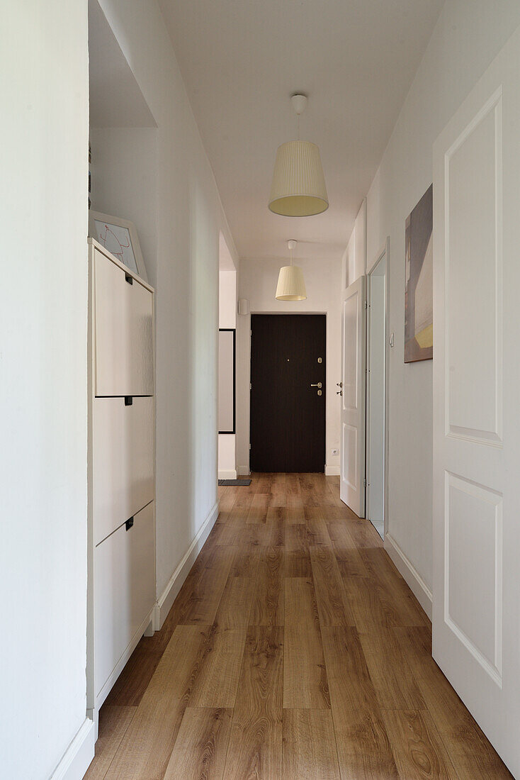 Long hallway with wooden floor and white walls in a flat