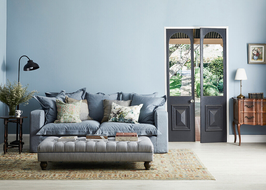 Living room with blue couch and light blue walls with glass door to the garden