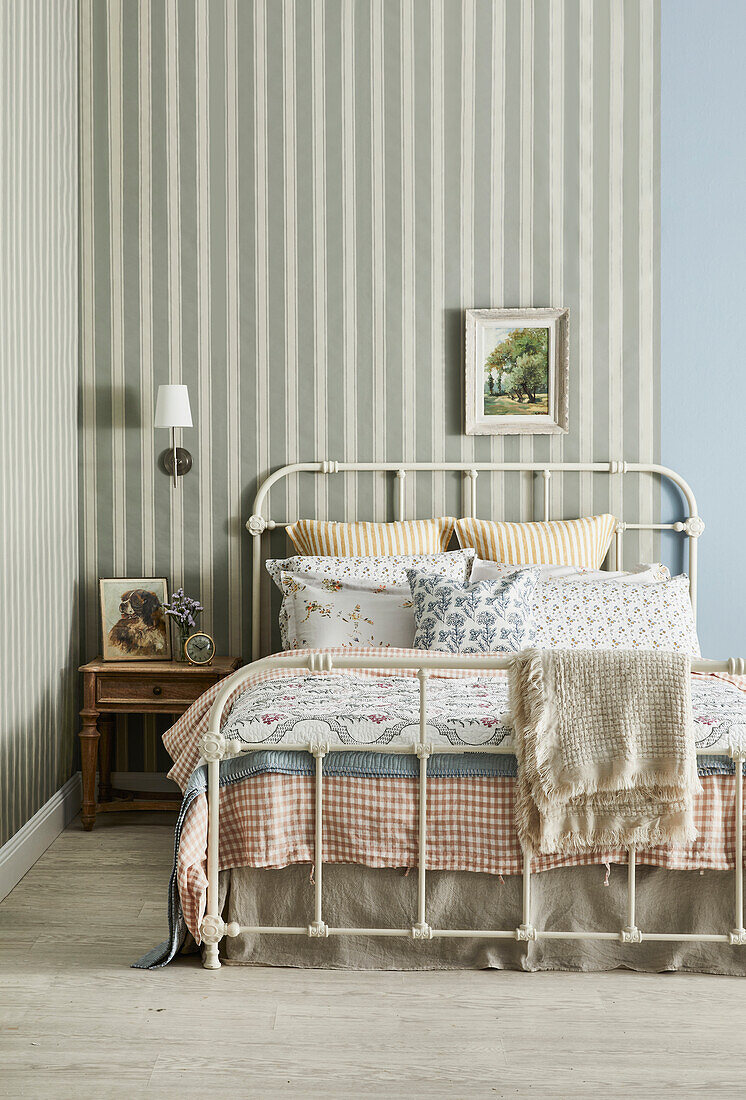 Metal bed with patterned pillows and blankets and striped wallpaper in the bedroom