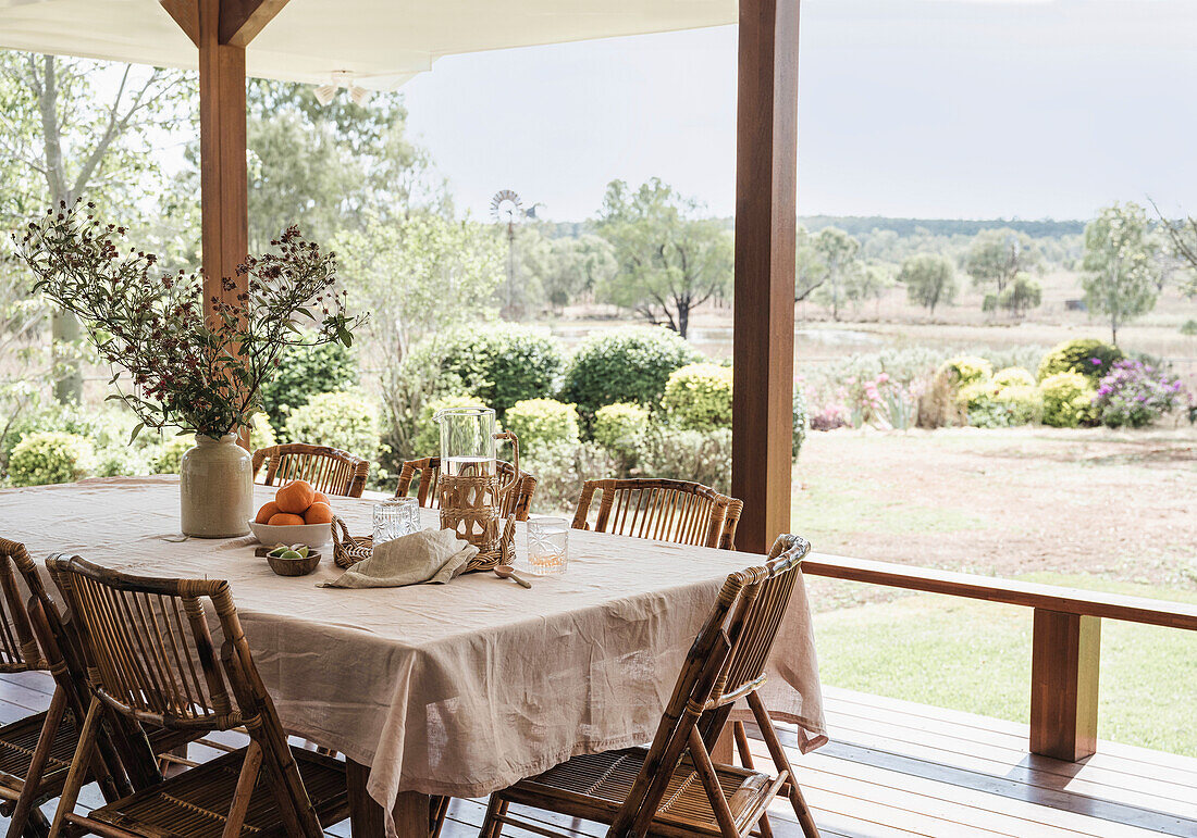 Set wooden table with linen tablecloth and rattan chairs on a porch