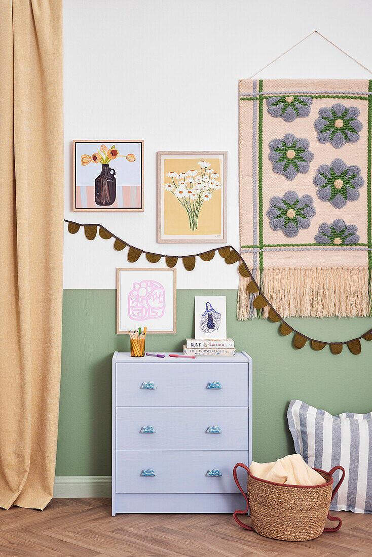 Colourfully decorated corner with chest of drawers, tapestry and pictures