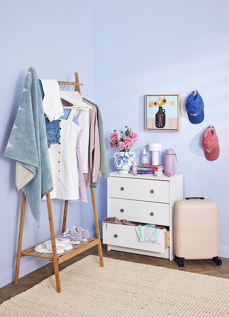 Corner with clothes rack, chest of drawers and suitcase in a pastel-coloured room