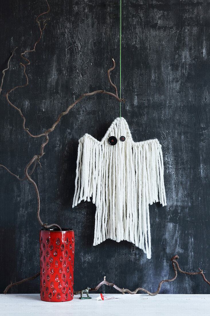 DIY wool ghost with button eyes in front of a dark wall