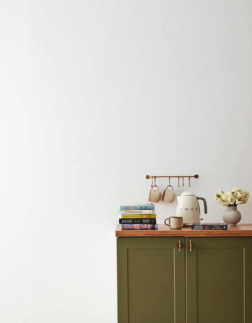 Green sideboard with kettle, cups, stack of books and flower arrangement