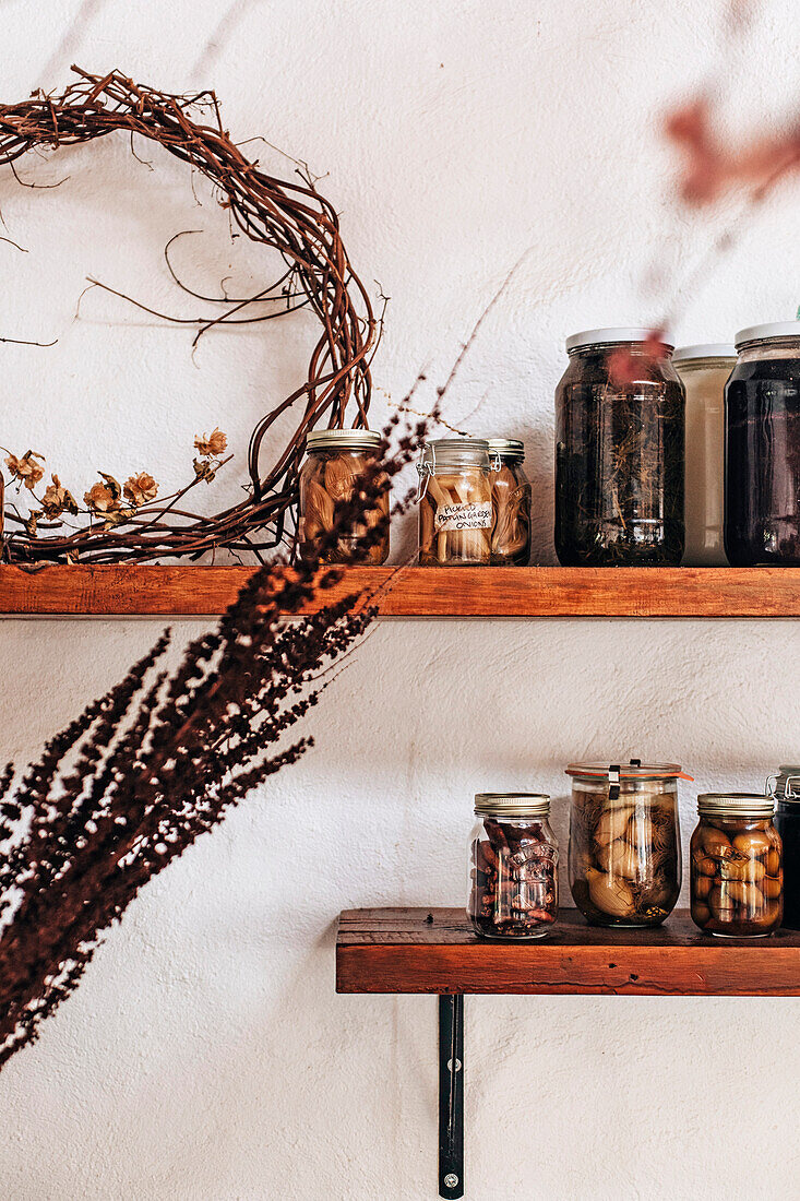 Shelves with preserving jars and dried flowers on a white wall