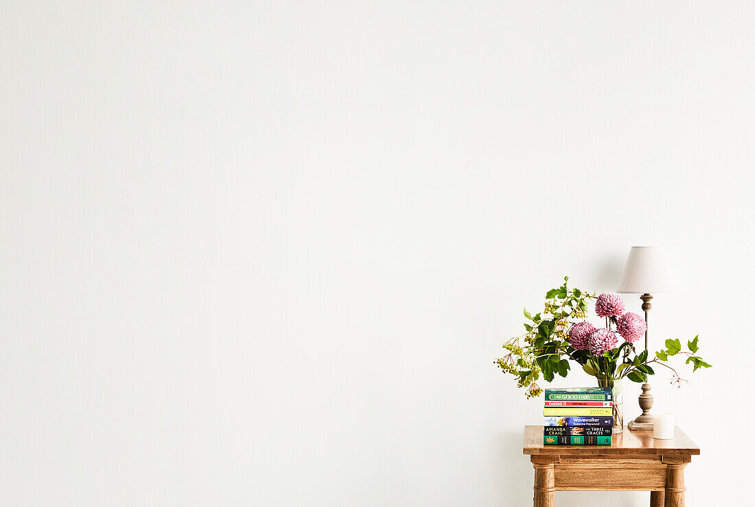 Kleiner Holztisch mit Blumenstrauß und Büchern vor weißer Wand