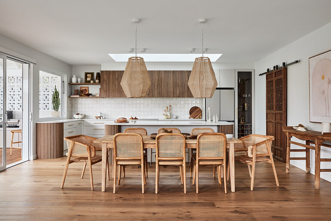 Dining area with wooden table and modern pendant lights, open kitchen in the background