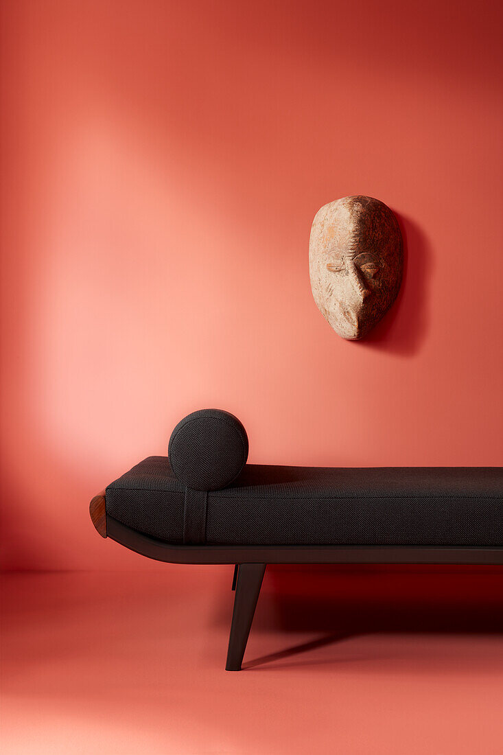 Black daybed in front of coral-coloured wall, stone mask