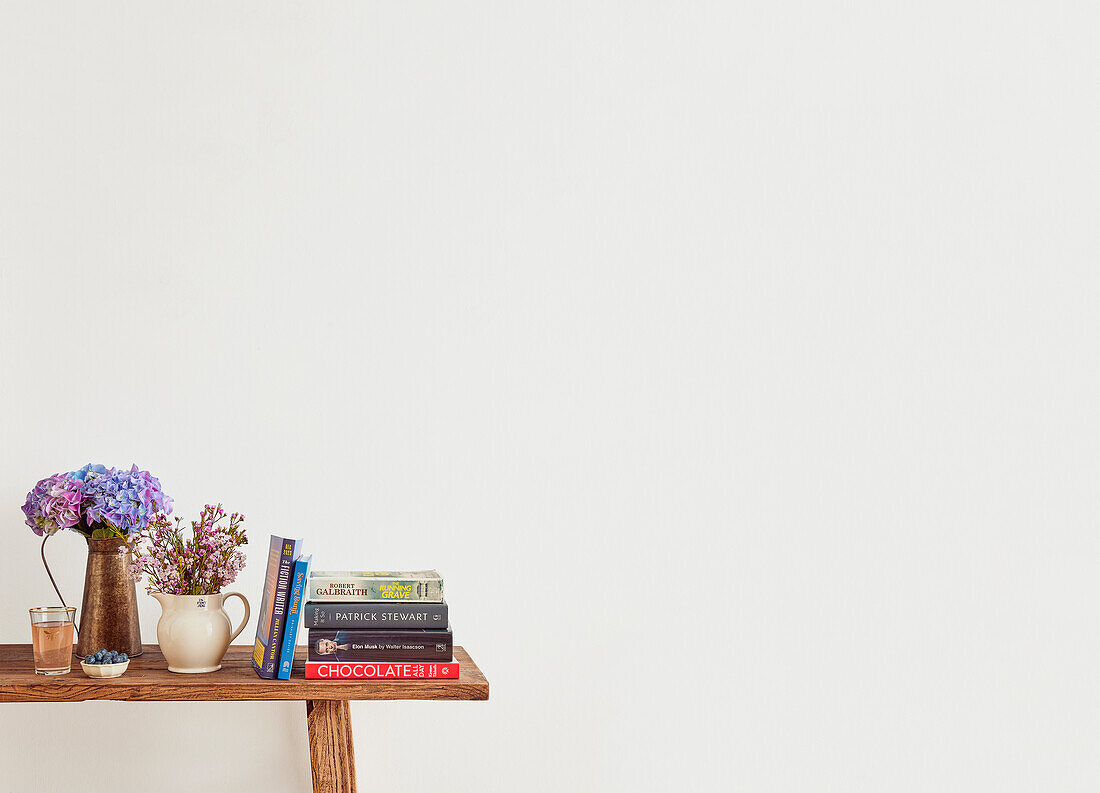 Holztisch mit Bücherstapel und Blumenvase im minimalistischen Raum