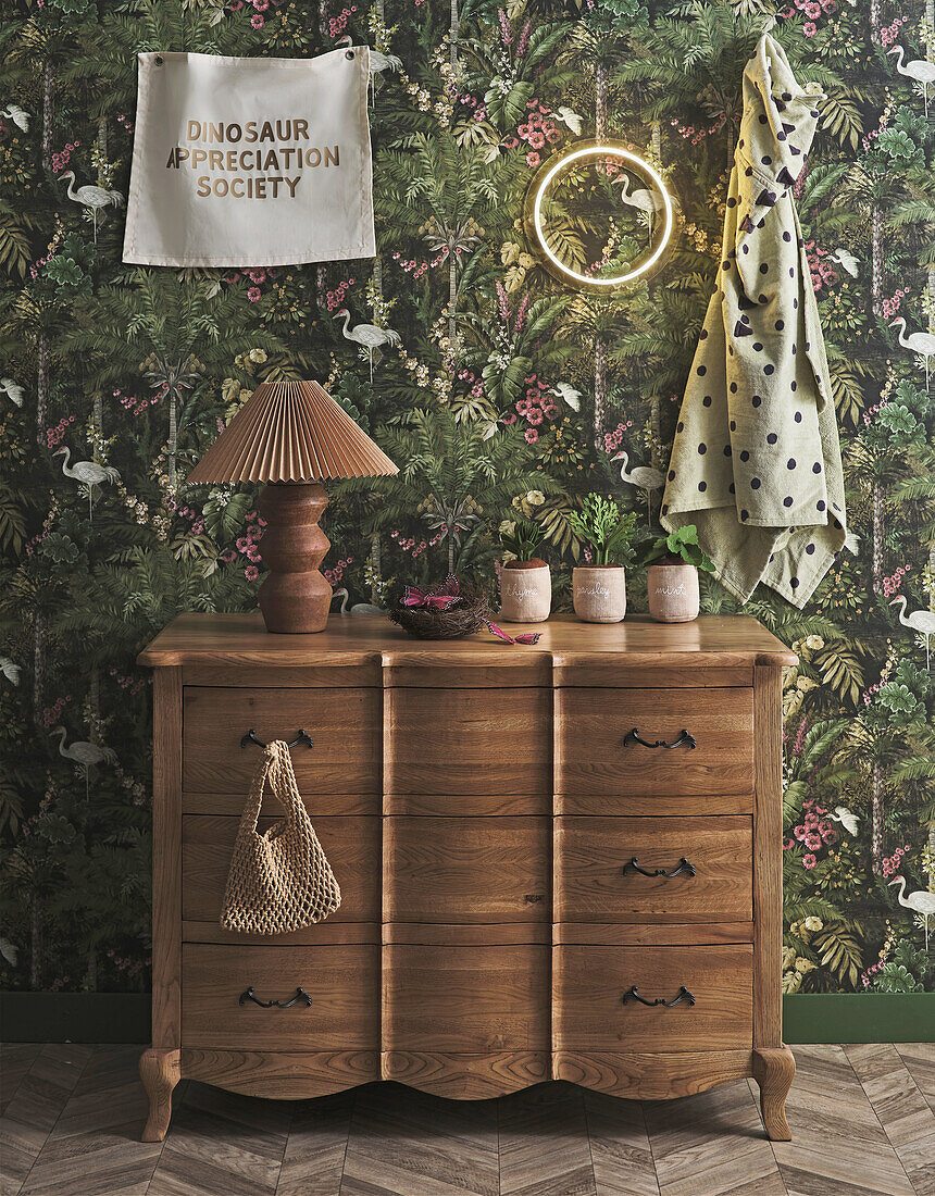 Wooden chest of drawers in front of jungle wallpaper with dinosaur poster and decorative elements