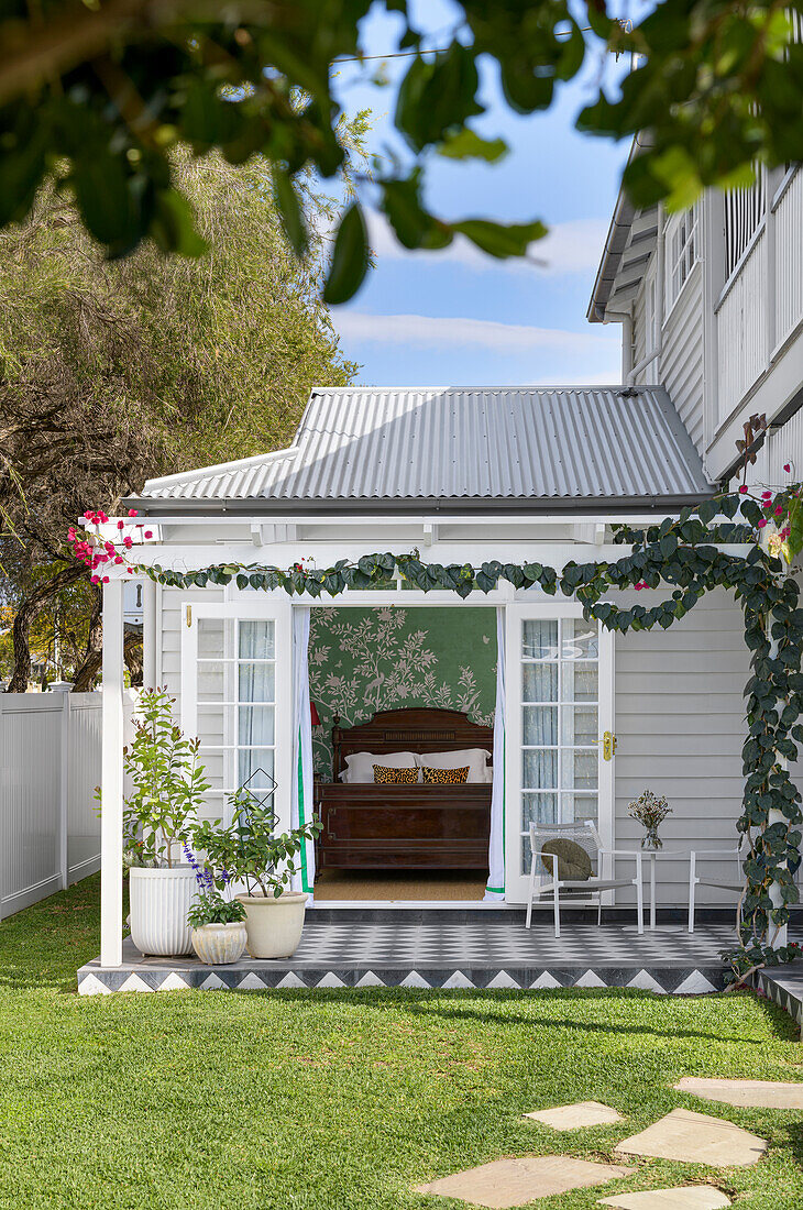 Veranda with flowering vines and view into bedroom with antique double bed