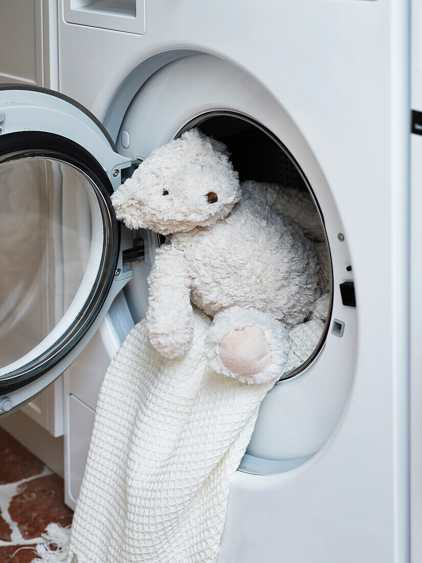 Kuschelweicher Teddybär und Handtuch in geöffneter Waschmaschine