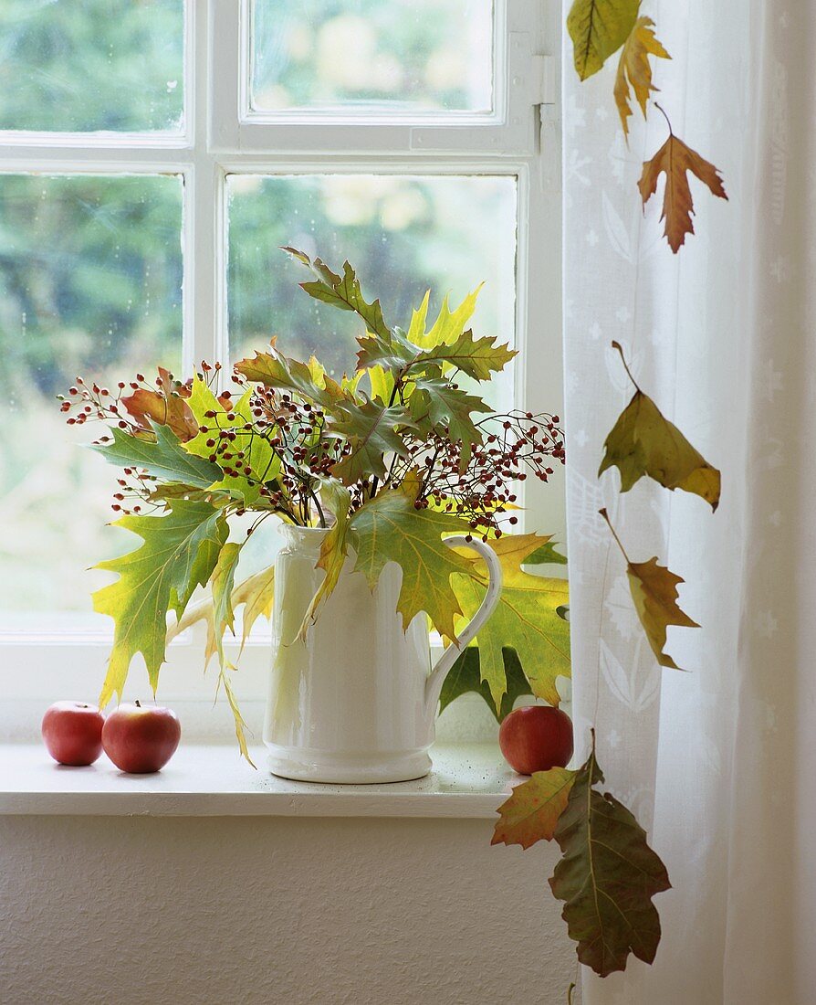 Herbststrauss mit Blättern und Hagebuttenzweigen im Fenster