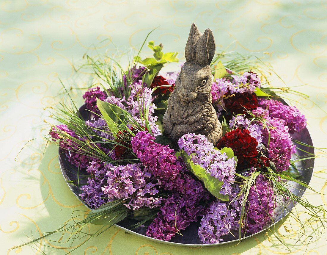 Blumenarrangement mit Flieder und Osterhase auf einem Teller