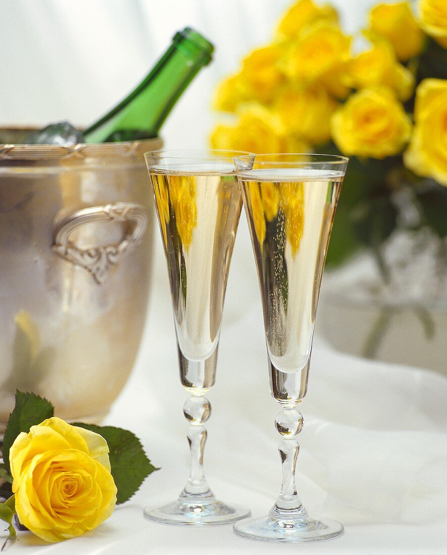 Zwei Gläser Sekt, Sektkübel mit -flasche und gelbe Rosen