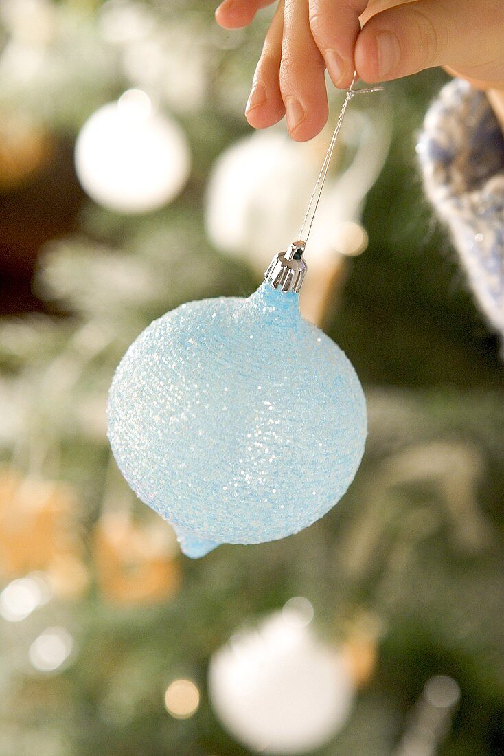 Child's hand holding a pale-blue Christmas bauble