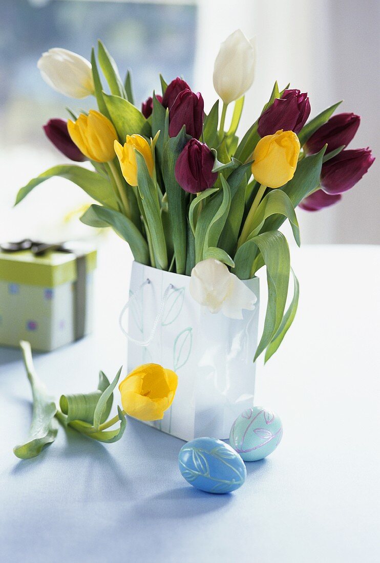 Colourful bunch of tulips in vase, Easter eggs in front