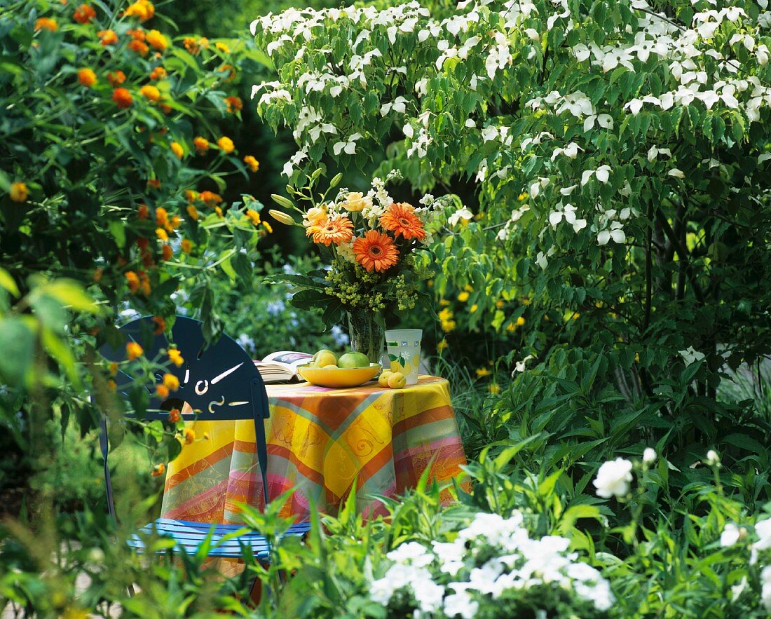 Tisch mit Obstschale, Blumenstrauss, Buch in blühendem Garten