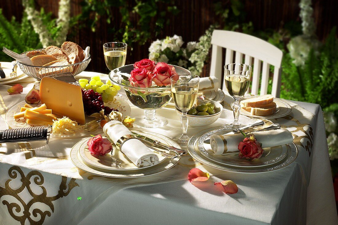 Gedeckter Tisch mit Rosenblüten, Käseplatte, Oliven etc.