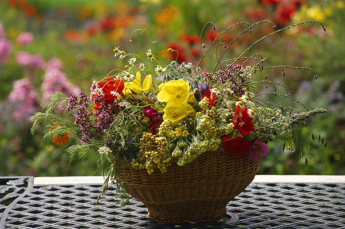 Sommerliches Gesteck mit Blüten und Gräsern in Korbschale