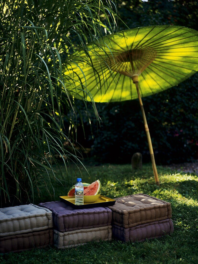 Melonenschnitze auf Kissen im Freien mit grünem Sonnenschirm