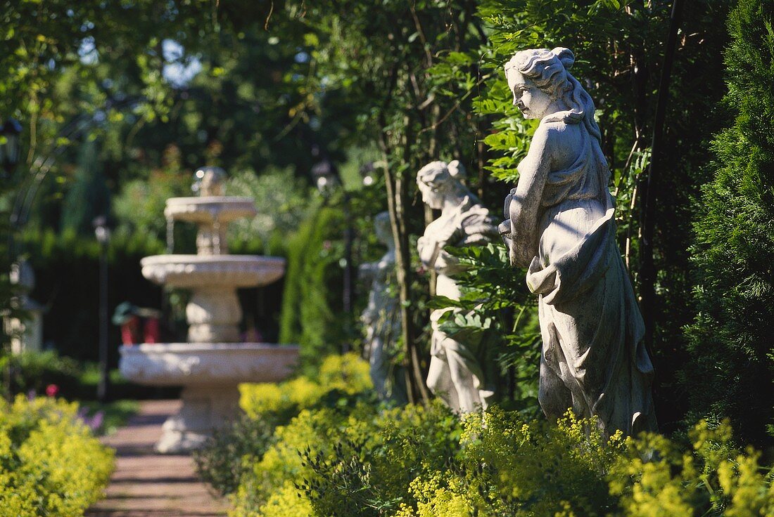 Blick in einen Garten mit Steinbrunnen und Steinfiguren